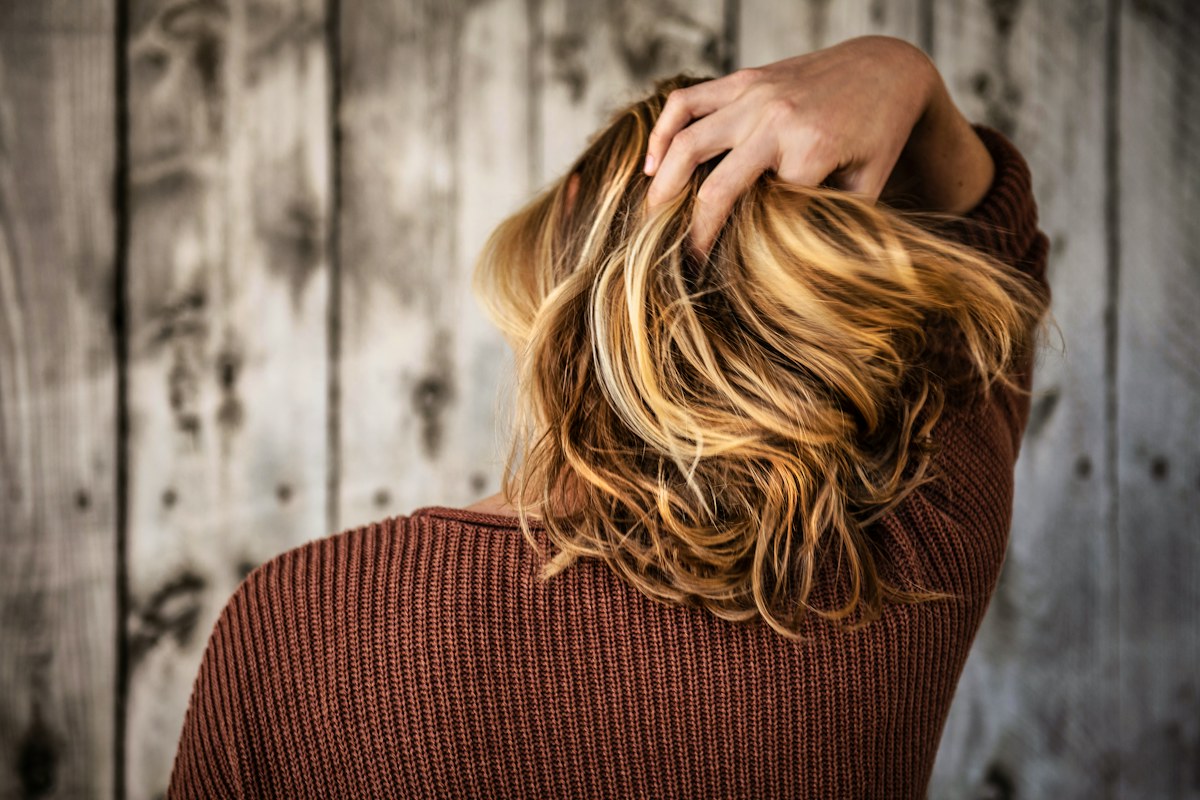 Женщина касается волос на затылке